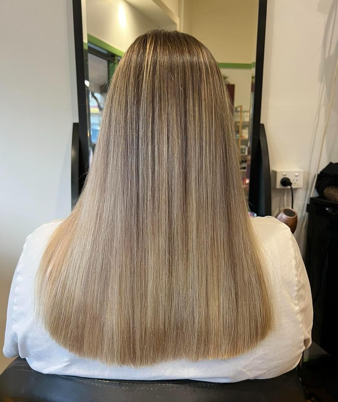 A Woman With Long Blonde Hair is Sitting in a Chair in Front of a Mirror — Choo Choo Hair and Beauty In Wyong, NSW