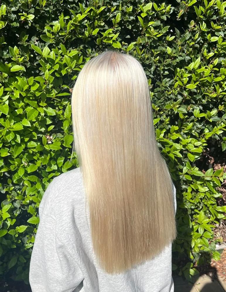 A Woman With Long Blonde Hair is Standing in Front of a Bush — Choo Choo Hair and Beauty In Wyong, NSW