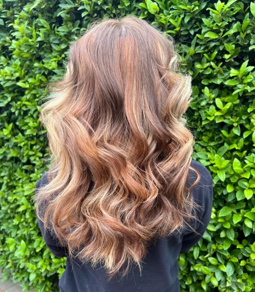 A Woman With Long Brown Hair is Standing in Front of a Hedge — Choo Choo Hair and Beauty In Wyong, NSW A Woman With Long Brown Hair is Standing in Front of a Hedge — Choo Choo Hair and Beauty In Wyong, NSW