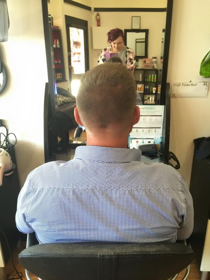 A Man in a Blue Shirt is Sitting in a Chair in Front of a Mirror — Choo Choo Hair and Beauty In Wyong, NSW