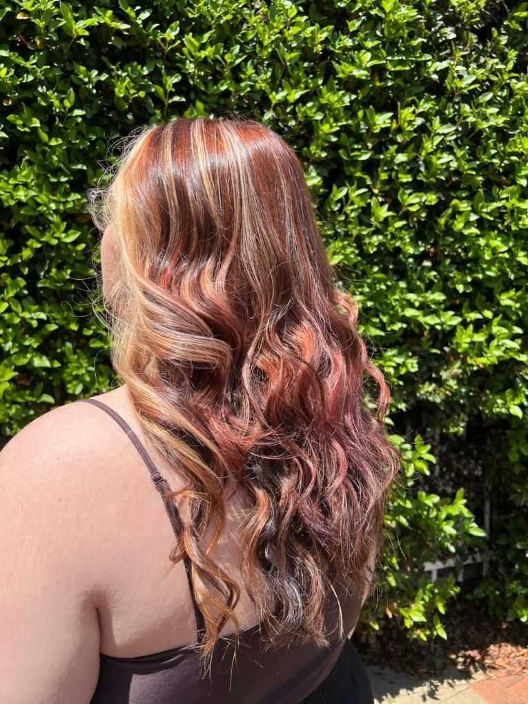 A Woman With Long Brown Hair is Standing in Front of a Bush — Choo Choo Hair and Beauty In Wyong, NSW