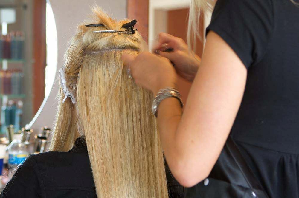 Stylist Applying Hair Extensions to a Long Blonde Hairstyle in a Salon — Elysian Salon In Wyong, NSW