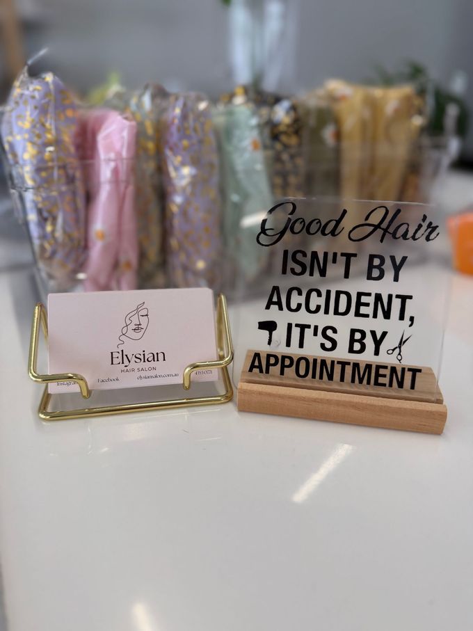 A Woman With Long Brown Hair is Standing in Front of a Hedge — Choo Choo Hair and Beauty In Wyong, NSW Hair products in clear pouches beside a sign reading, “Good hair isn’t by accident, it’s by appointment.” — Elysian Salon In Wyong, NSW