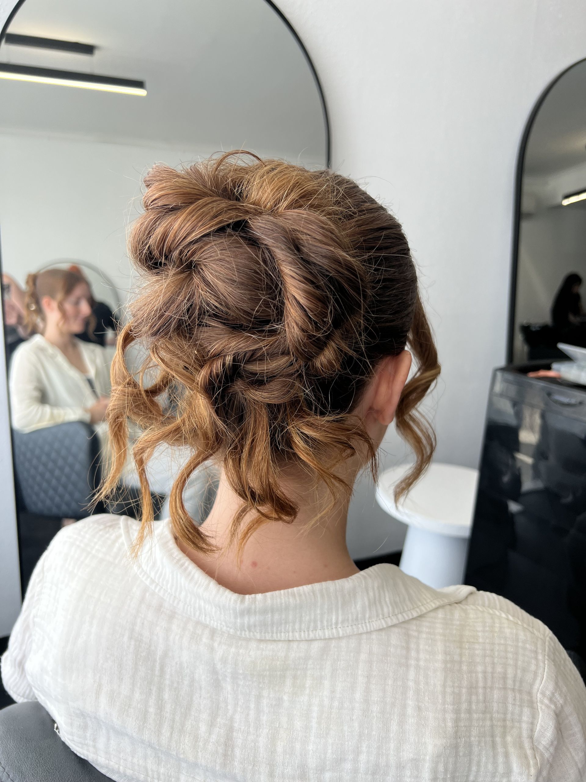 Back of a person with curly hair pinned up, wearing a white top in a salon mirror area — Elysian Salon In Wyong, NSW