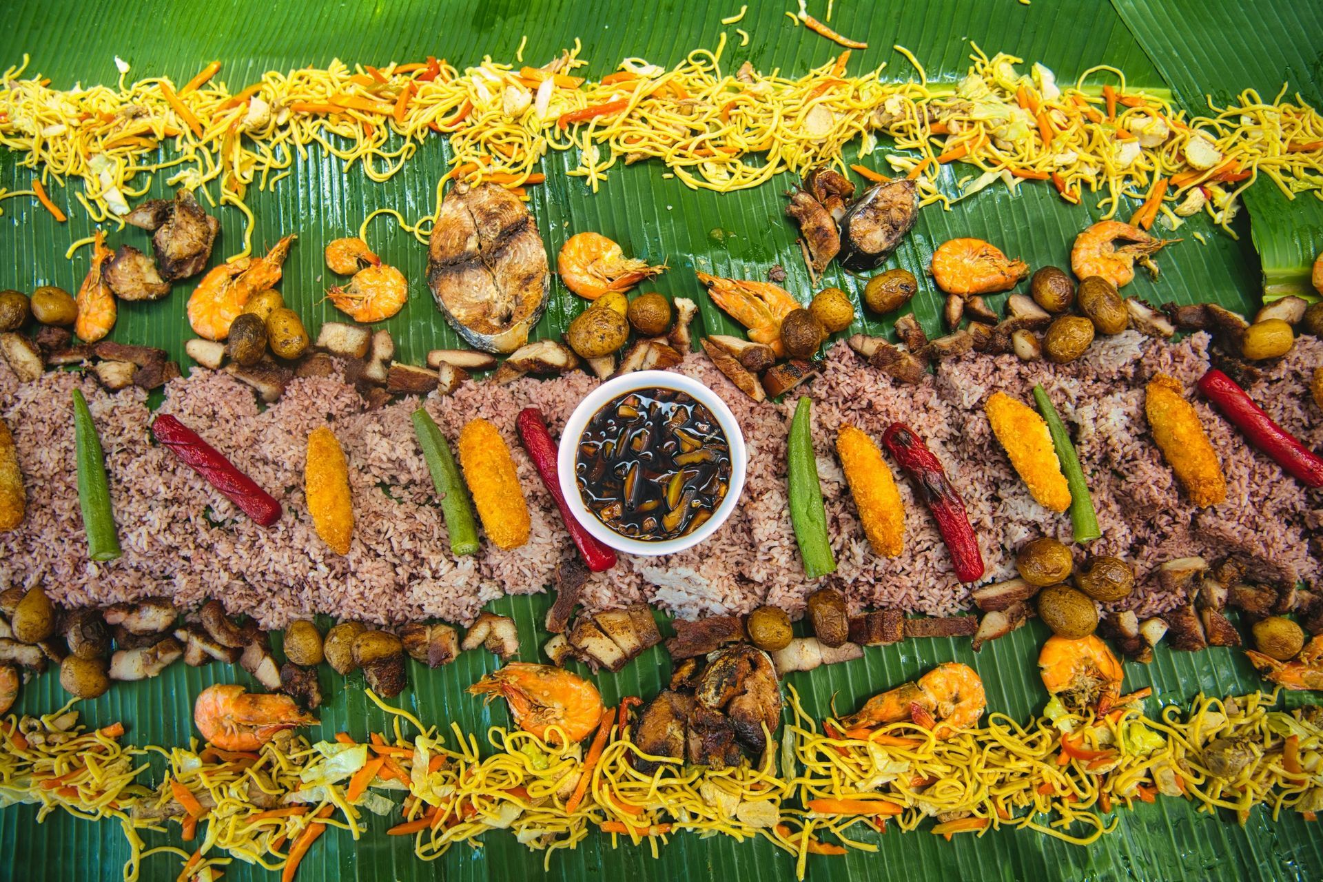 A Filipino Boodle Fight feast on banana leaves, with rice, seafood, vegetables, and sauce.