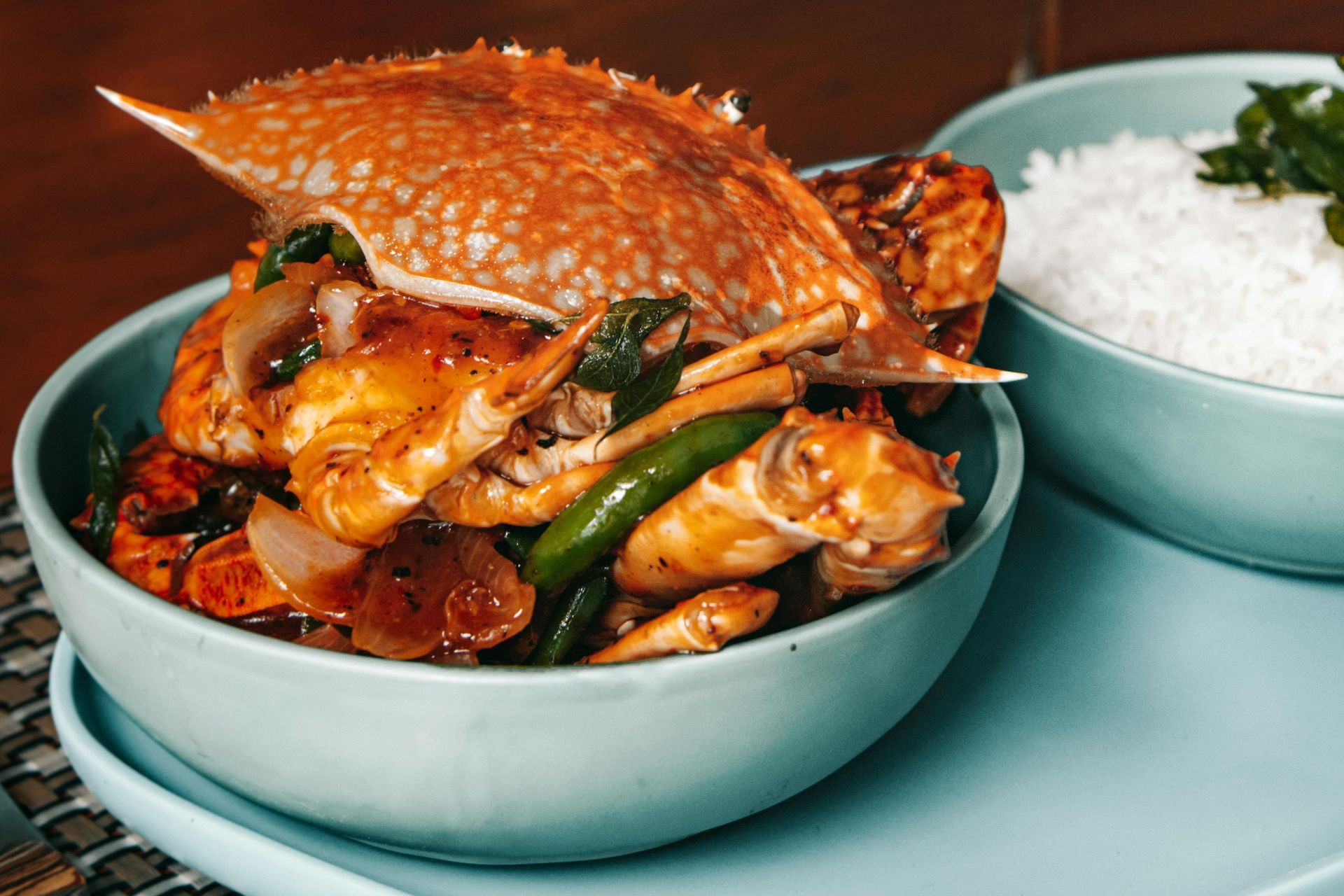 Crab dish with a red shell and vegetables in a teal bowl, served with rice.