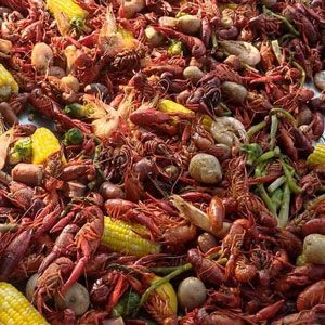 Crawfish boil: red crawfish, corn, potatoes, sausage, and vegetables in a large pile.