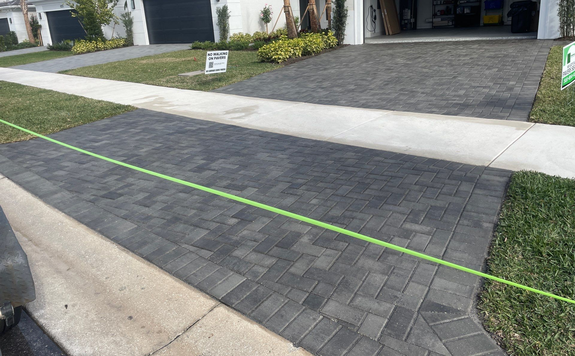 Brick driveway in front of a house, with green grass and sidewalk.