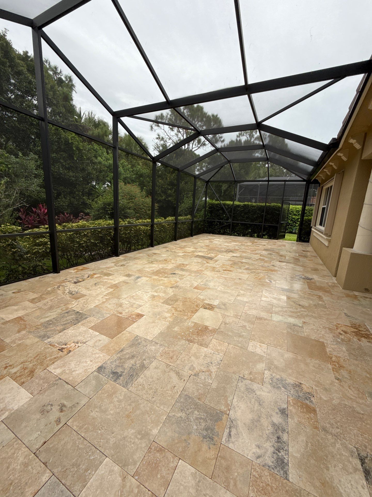Patio with brown tile, a pool, and greenery in a sunny outdoor setting.