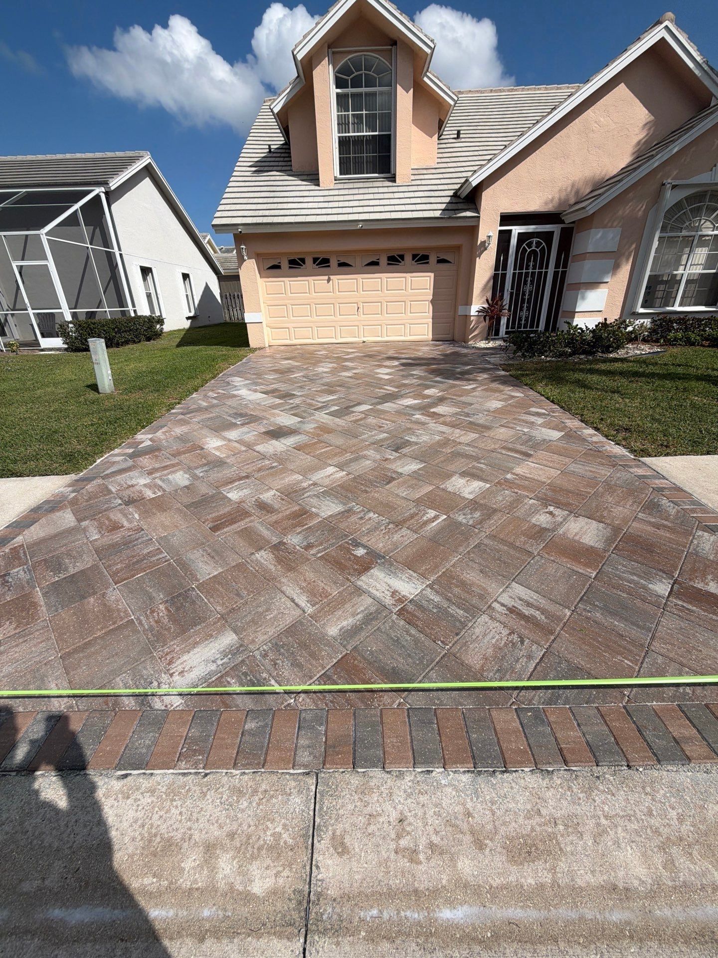 Brick paver driveway in front of a light peach house with beige garage door, and a grass lawn.