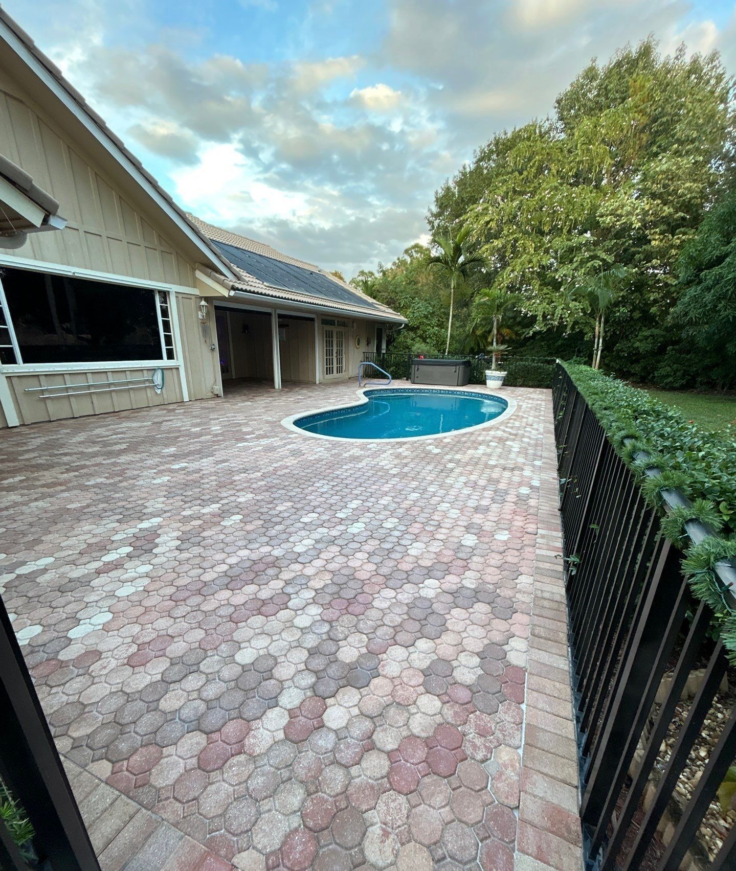 Brick patio with pool, surrounded by fence and house, under a cloudy sky.