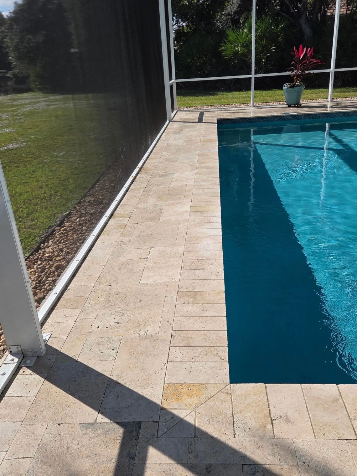 Poolside with stone pavers, pool water, and screened enclosure.