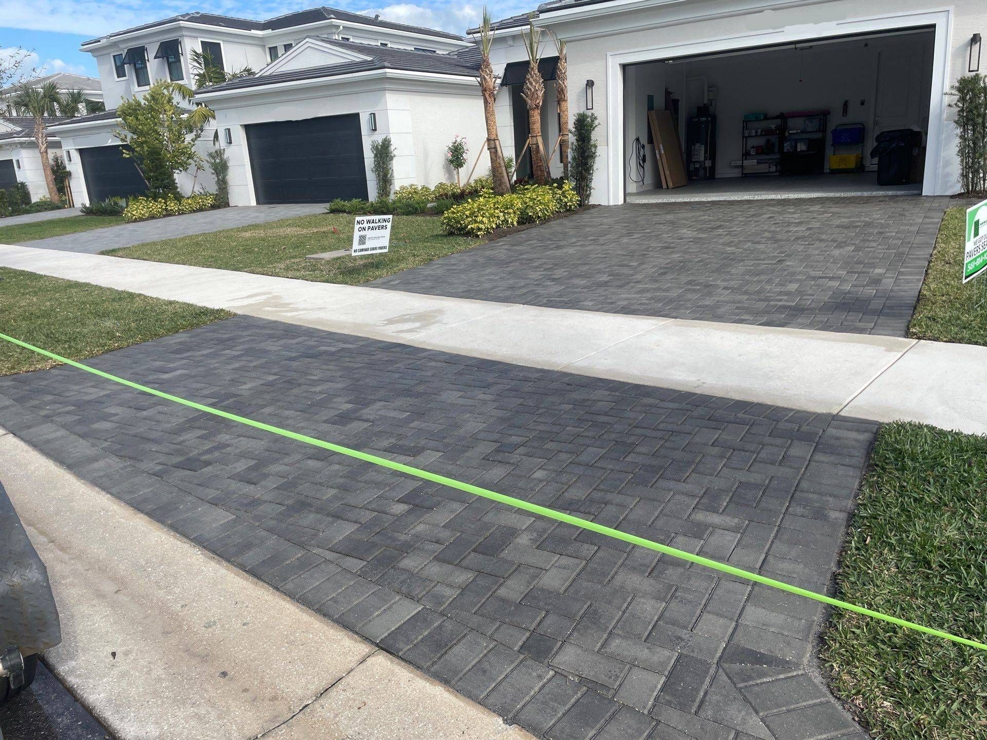 Brick driveway in front of a modern home, with a green lawn and two-car garage.