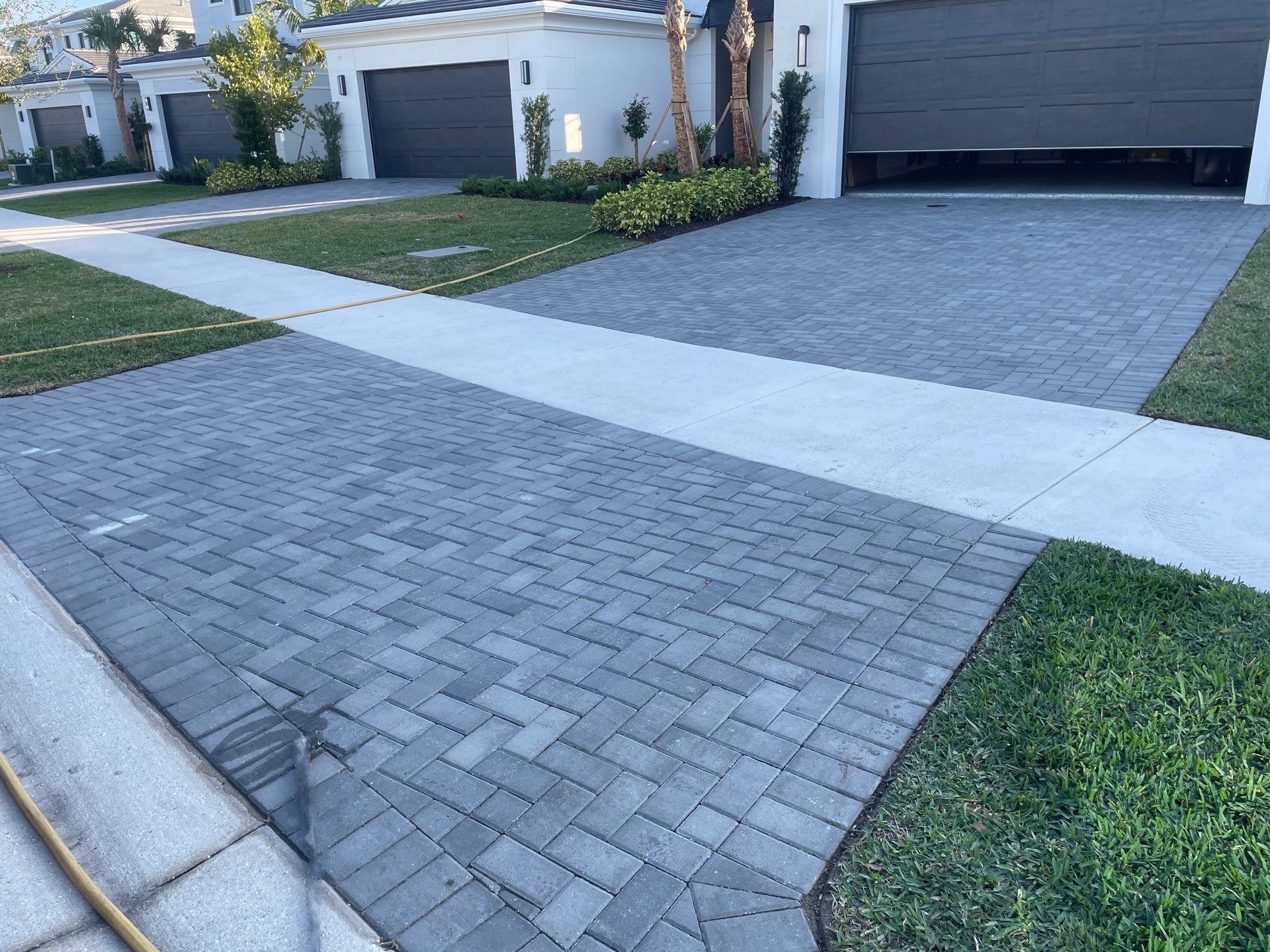 Paver brick driveways in front of white houses with green grass and gray garage doors.