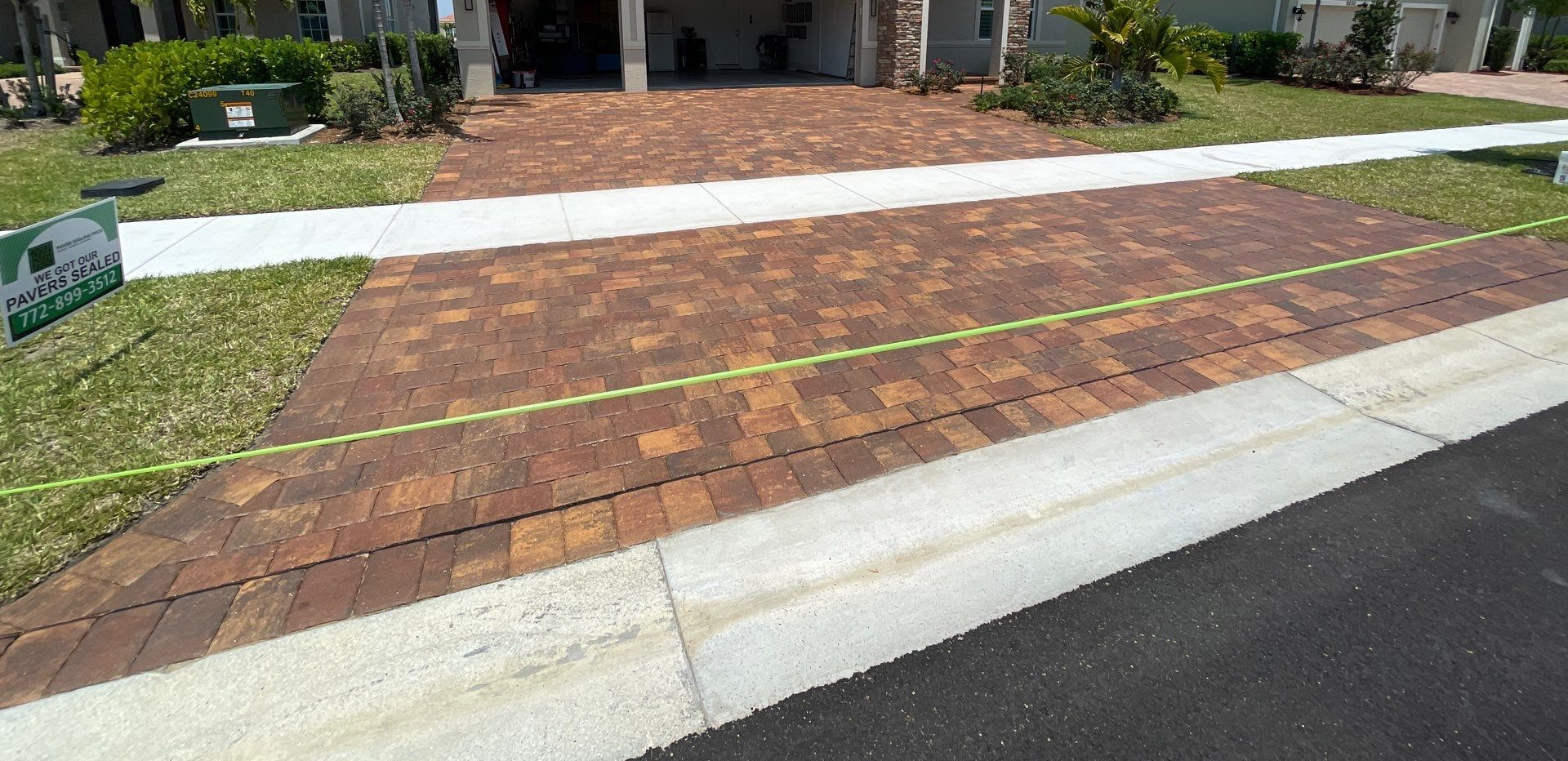 Brick driveway with green grass and a sidewalk. The street is to the right.