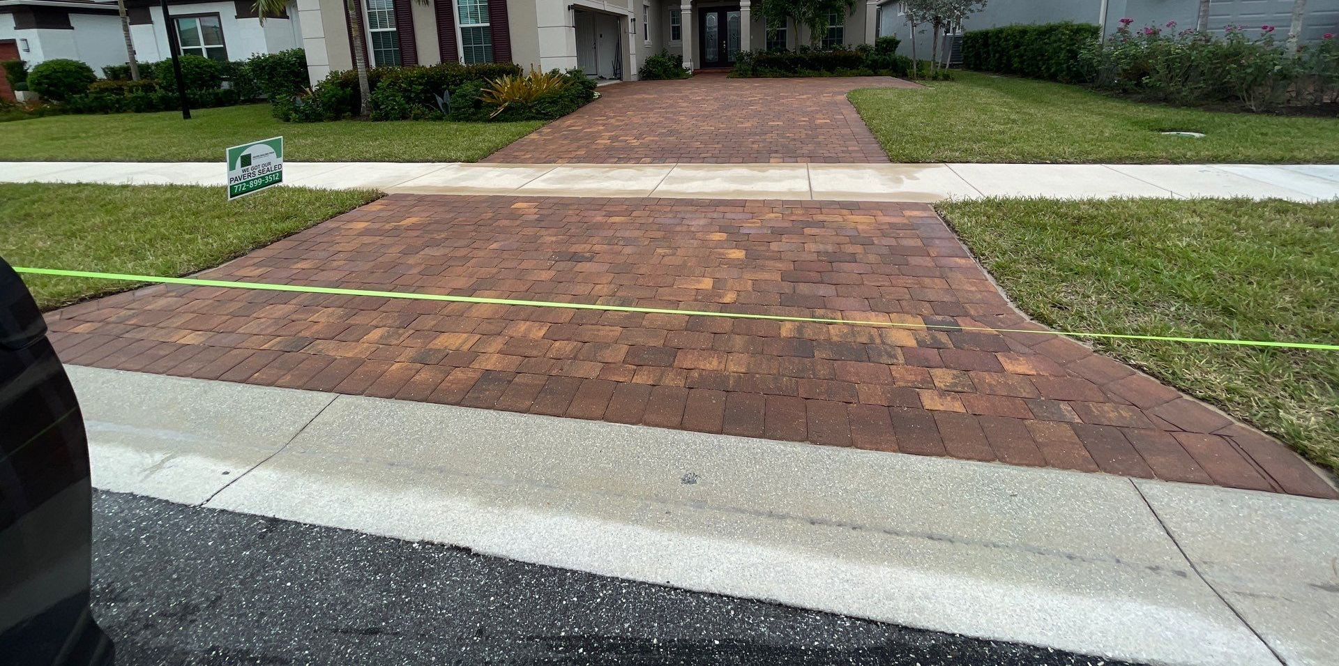 Brick driveway leading to a house with a green lawn.