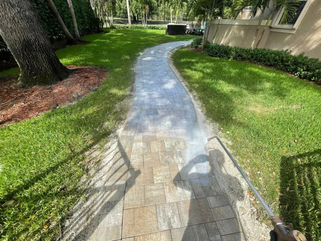 Power washing a stone path in a grassy yard, the person's shadow is visible.