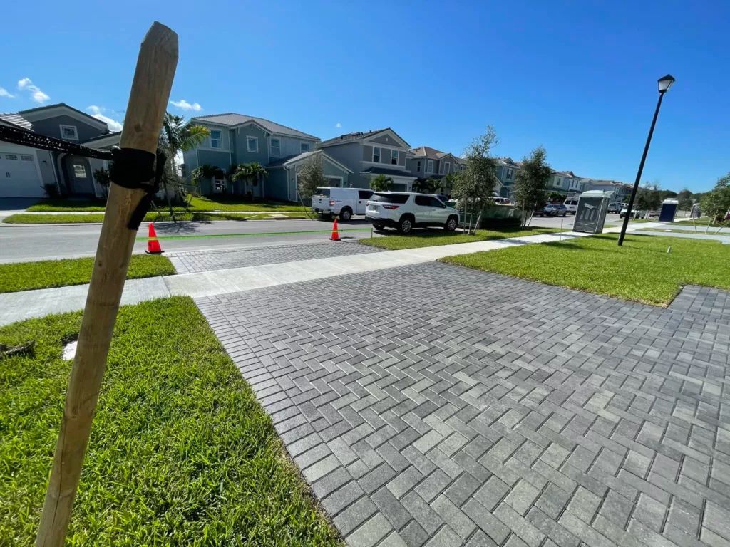 Paved driveway and street with green lawns and houses. A wooden pole is in the foreground. Bright blue sky.