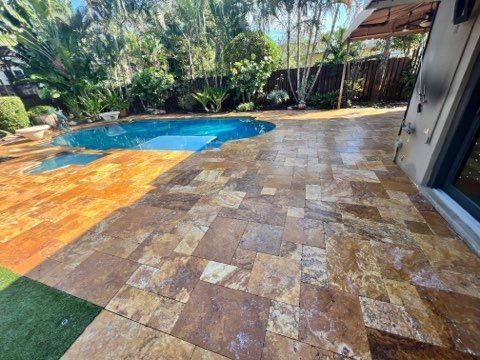 Patio with stone pavers and a pool; trees and greenery in the background.