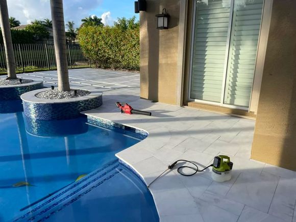 Poolside patio with pool. A leaf blower and a sprayer on the pavers.
