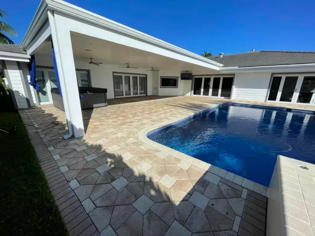 Backyard with pool, patio, and white house under a clear blue sky.