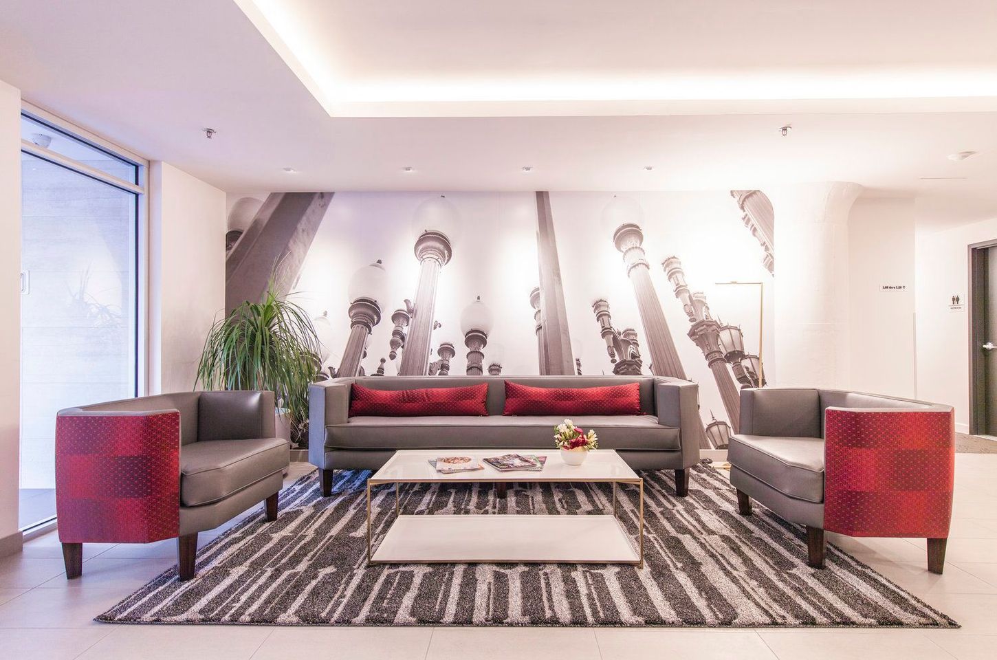 Lounge area with gray and red furniture, large print on the back wall, and a striped rug.