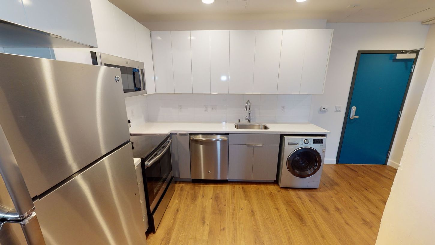 Modern kitchen with stainless steel appliances, white cabinets, and a turquoise door.