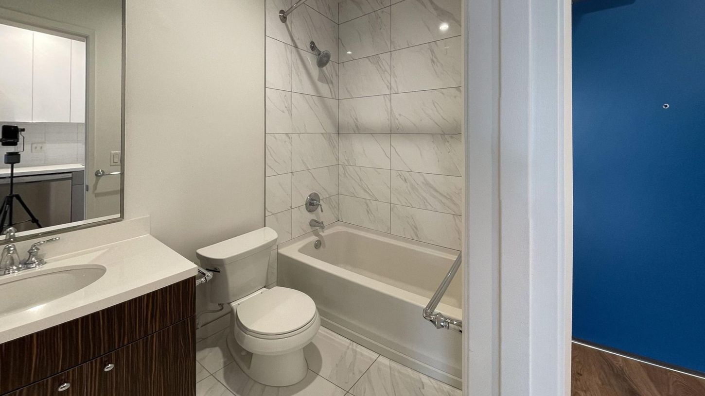 Bathroom with white marble tile shower, toilet, sink, and dark wood vanity. Blue wall visible.