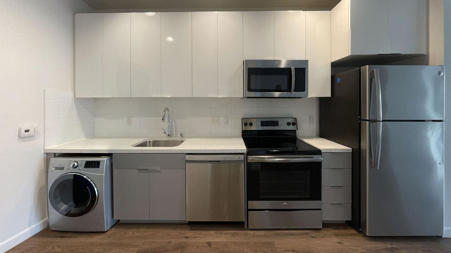 A modern kitchen with white cabinets, stainless steel appliances, and a washing machine.
