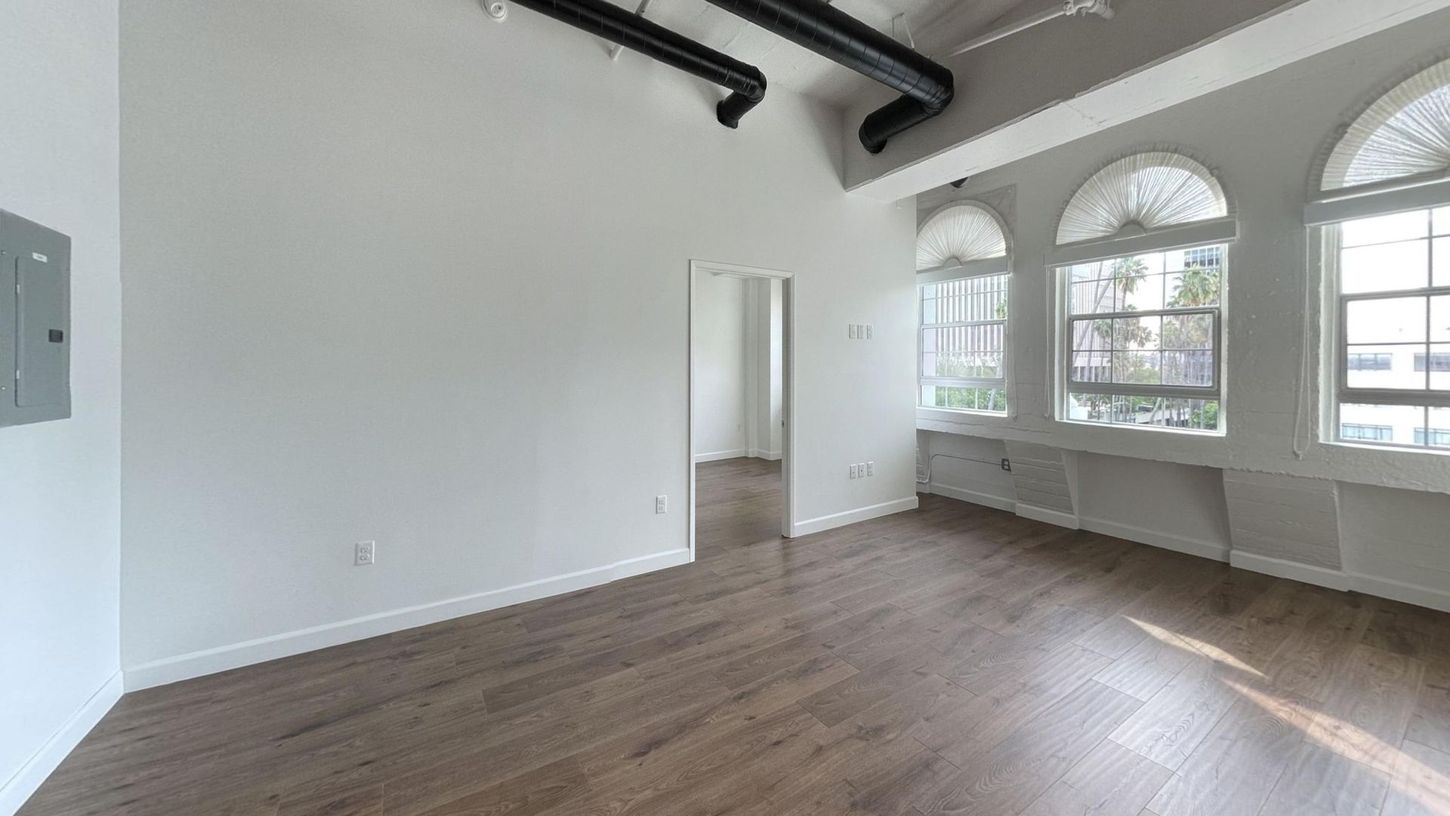 Empty loft apartment with arched windows and wood floors. White walls and exposed ductwork.