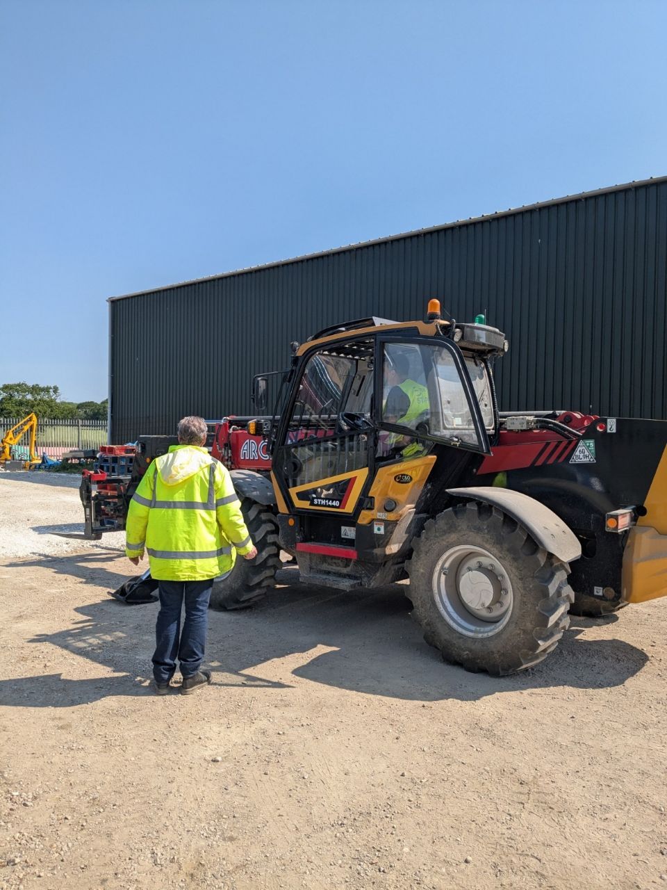 A man in a yellow jacket is standing next to a telehandler