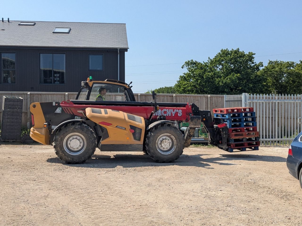 A red and yellow telehandler is parked in a parking lot next to a building.