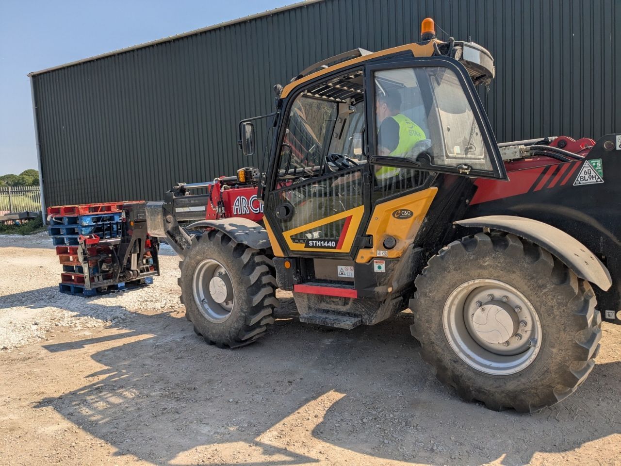 A yellow and red telehandler is parked in front of a building.