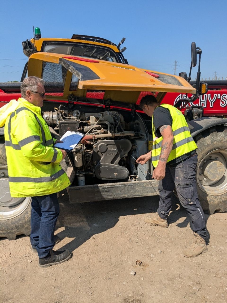 Two men in yellow vests are working on a telehandler.