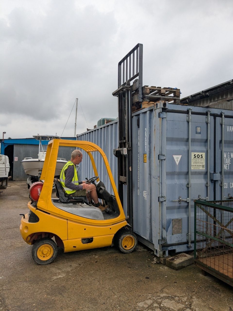 A man is driving a yellow forklift next to a blue container