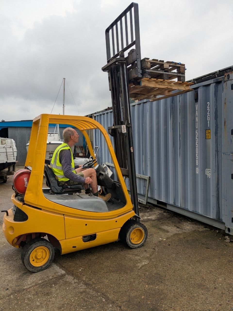 A man is driving a yellow forklift in a parking lot.