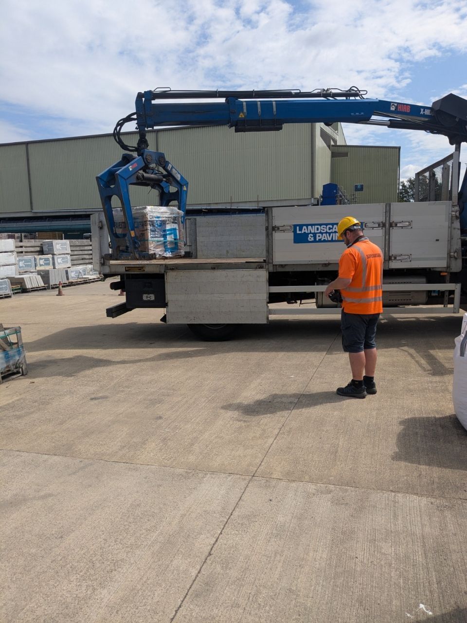 A man in an orange vest is standing next to a truck with a crane attached to it.