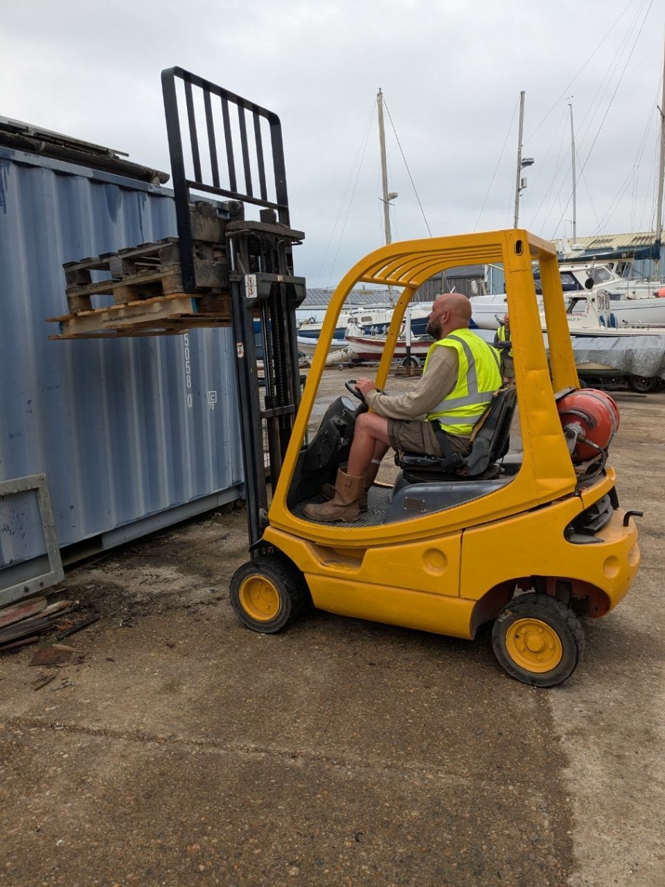 A man is driving a yellow forklift in a parking lot.