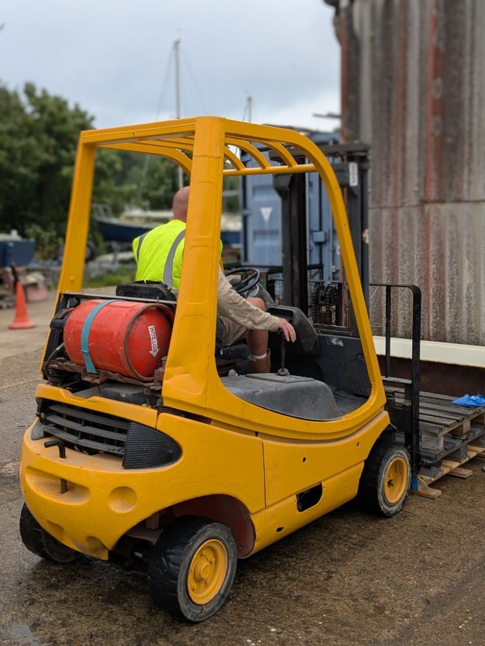 A man is driving a yellow forklift in a parking lot
