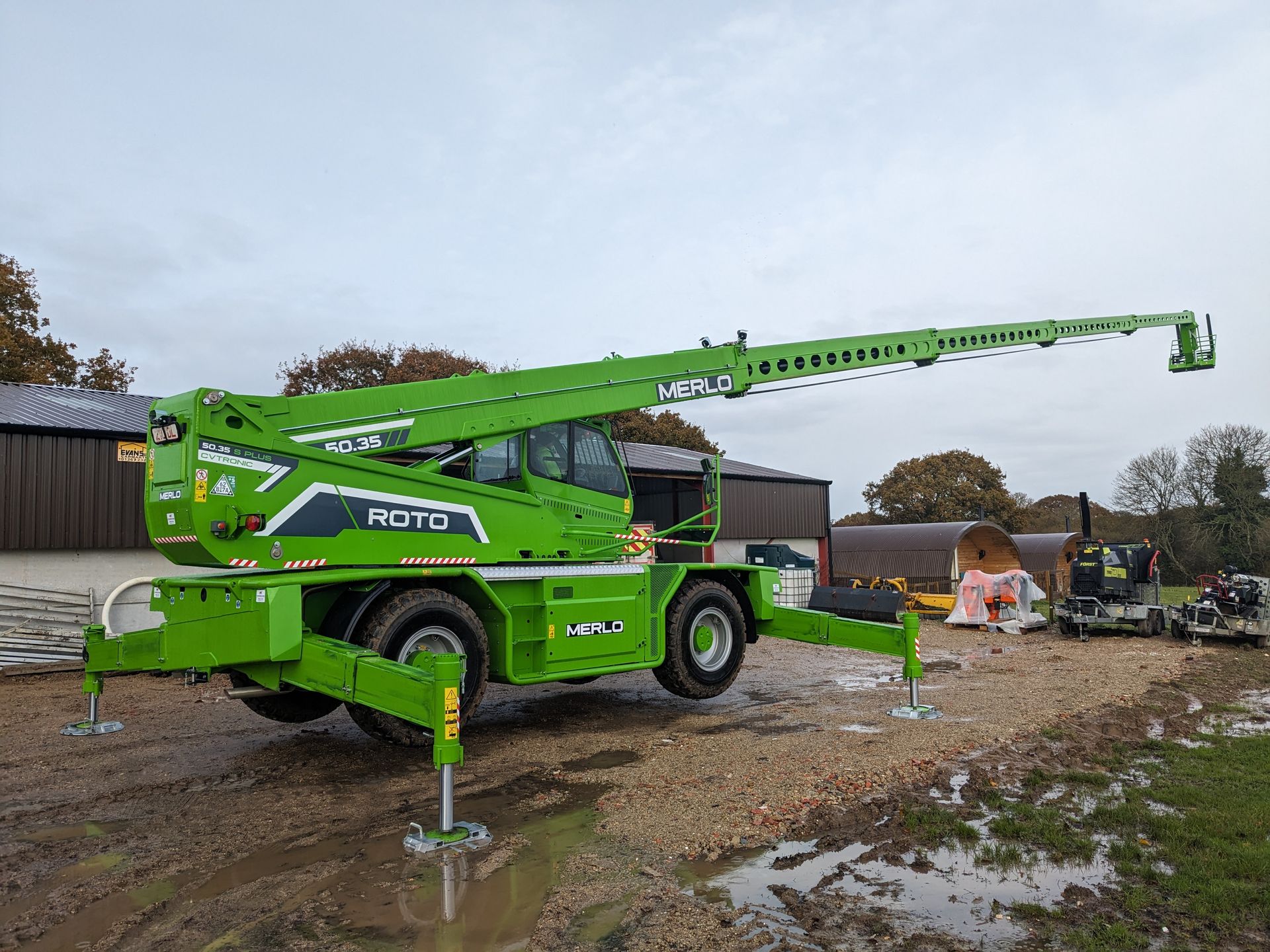 A green crane is parked in a muddy field.
