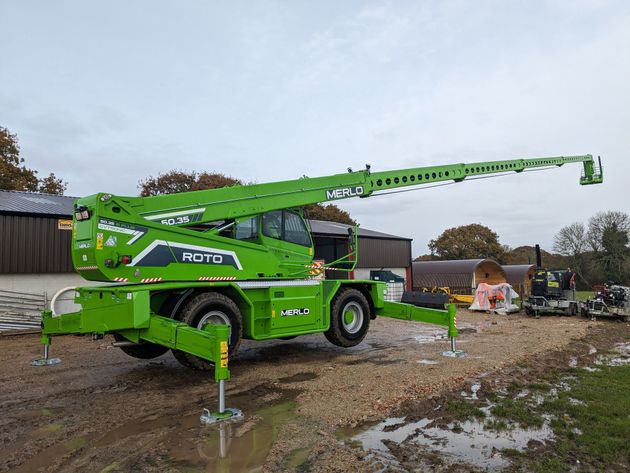 A green crane is parked in a muddy field.