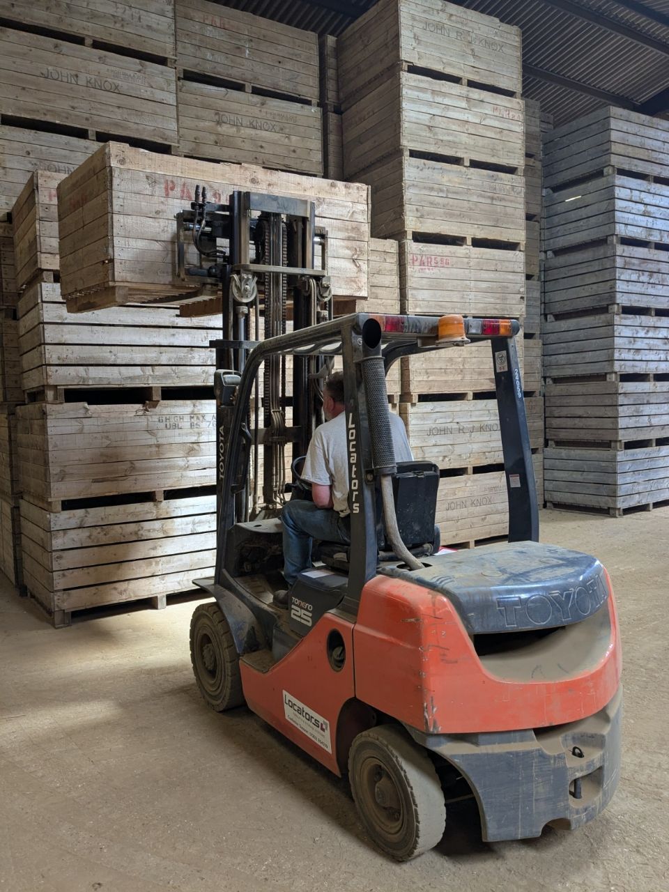 A man is driving a forklift in a warehouse filled with wooden crates