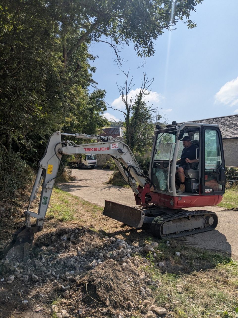 A man is driving a small excavator on a dirt road.