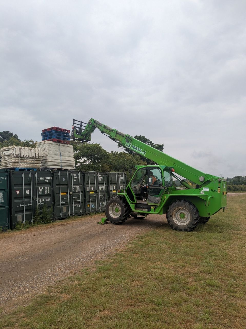 A green forklift is lifting a container in a field.