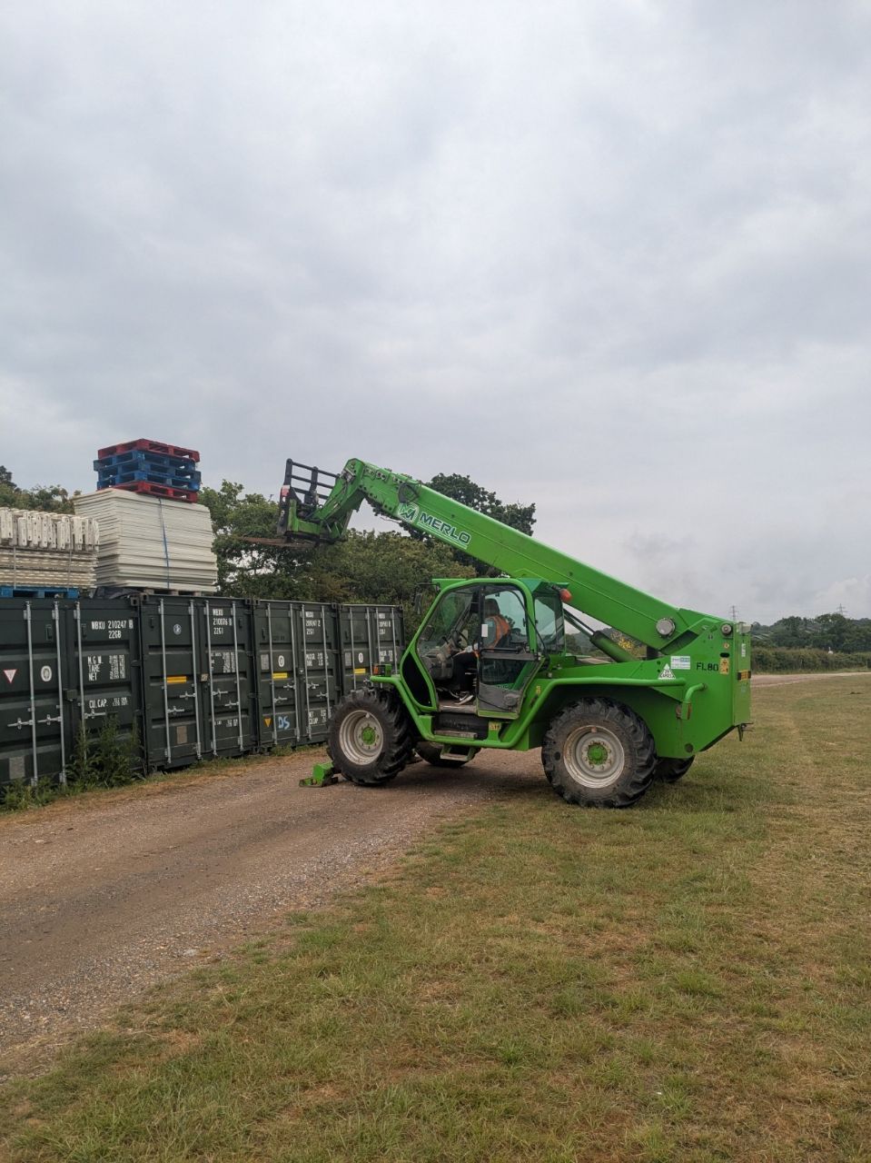 A green forklift is driving down a dirt road in a field.