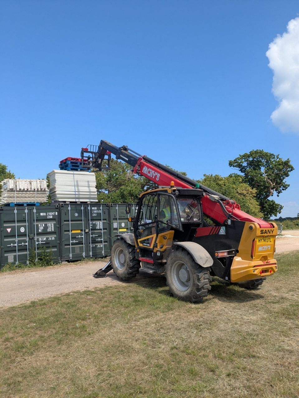 A red and yellow forklift is parked on the side of a dirt road.