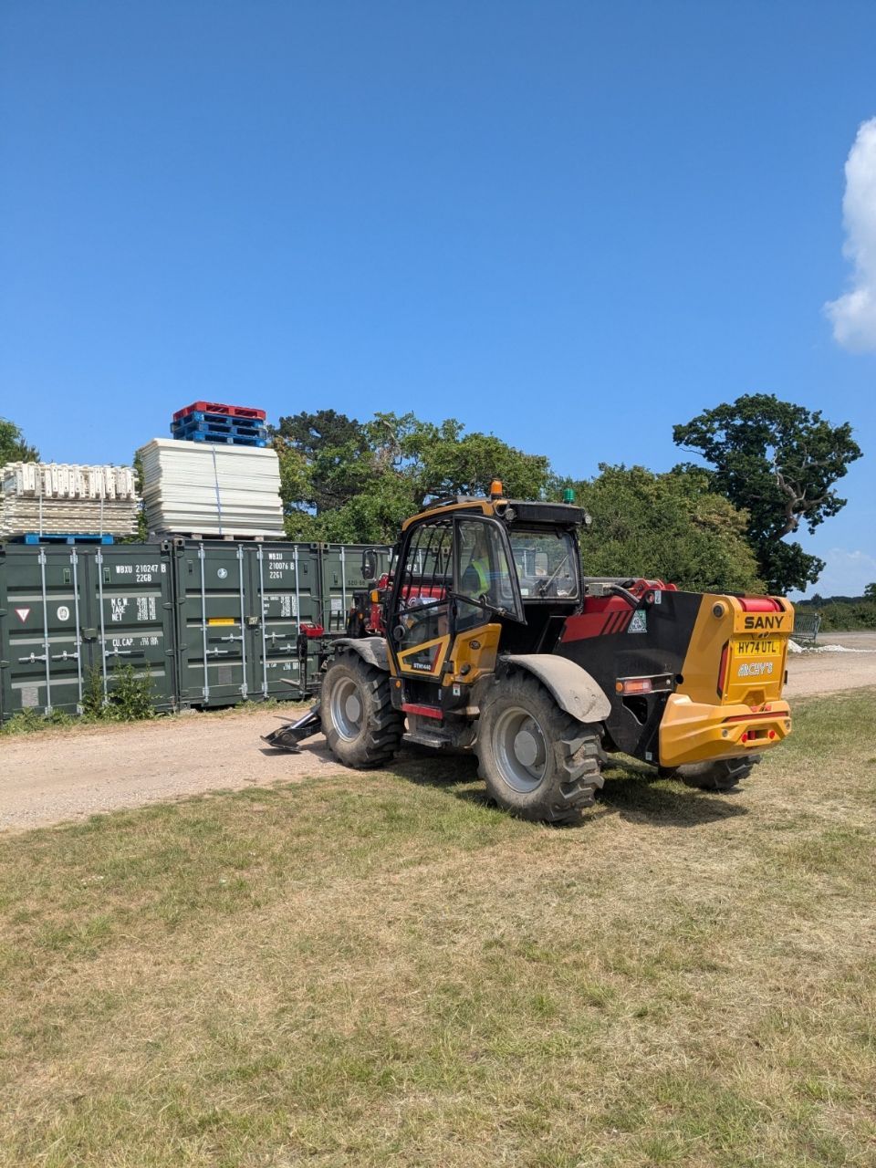 A forklift is parked on the side of a dirt road in a field.