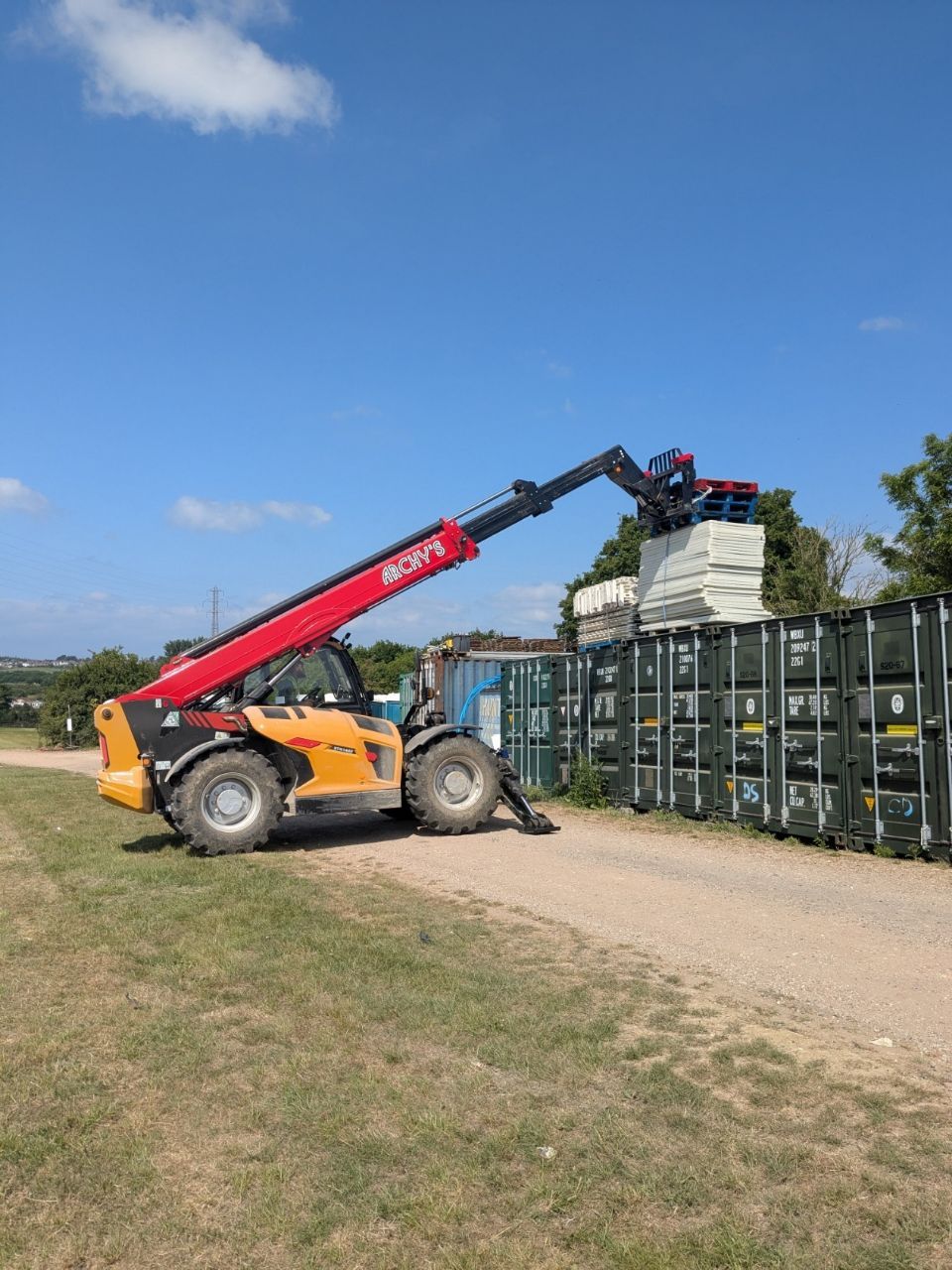 A forklift is carrying a stack of containers down a dirt road.