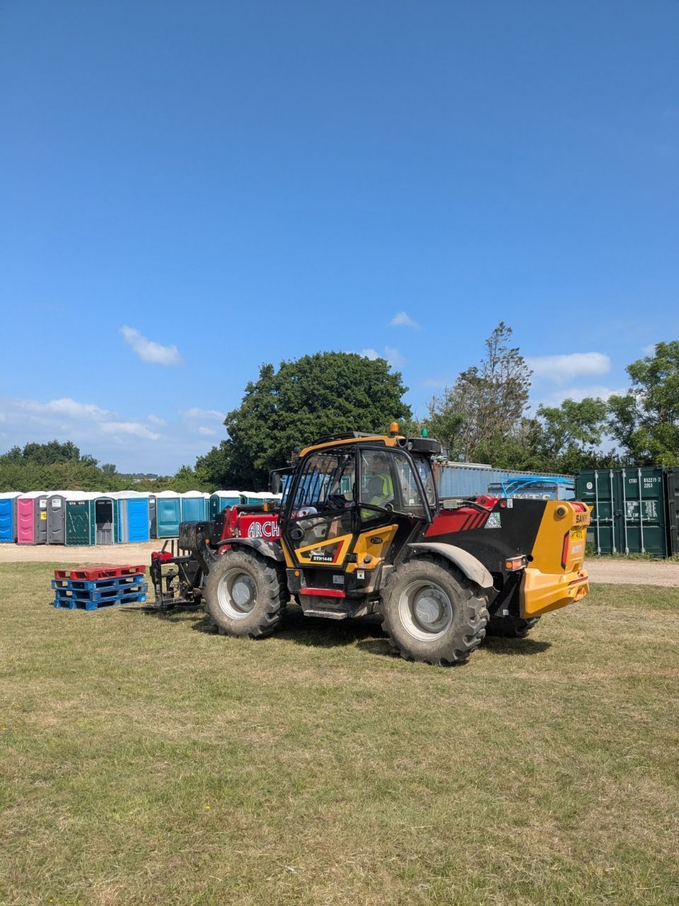 A yellow and black telehandler is parked in a grassy field.