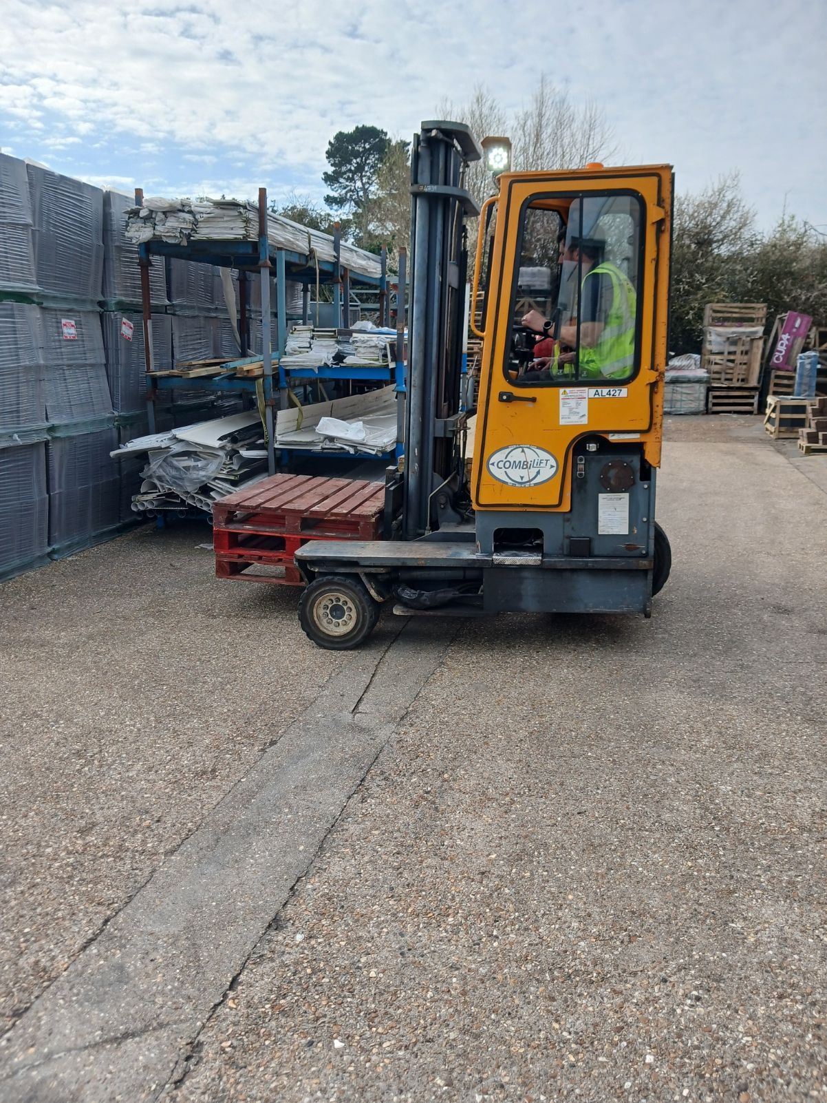 Yellow forklift in an industrial yard beside stacked materials and fencing